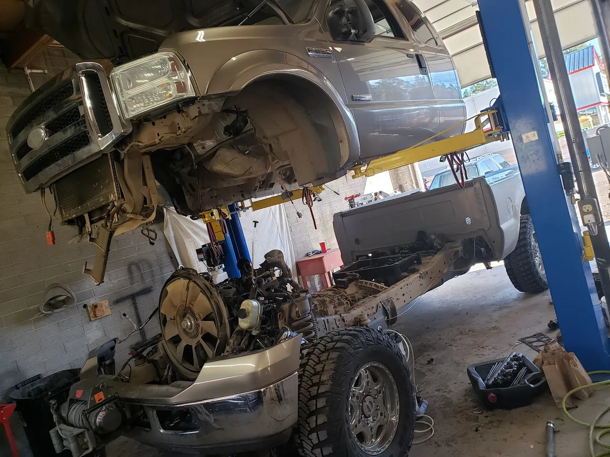A pickup on a two post lift inside the shop with its front end and body panels removed, the frame and suspension exposed.